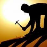 A silhouette of a man with a hammer in his hand, building a house roof
