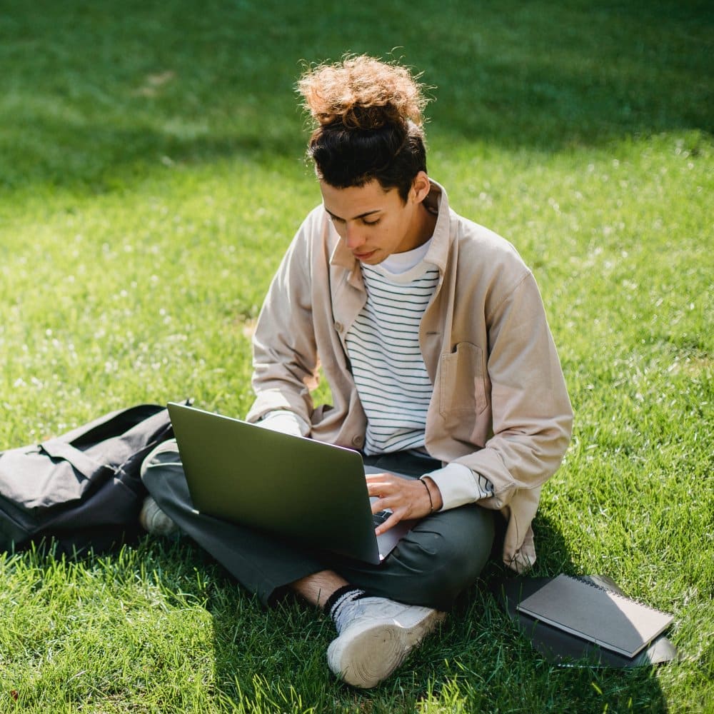 A young man using a laptop in a park.