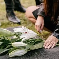 A girl laying down flowers on a graveyard.