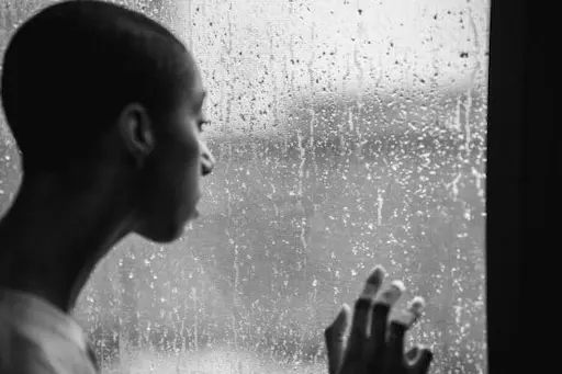 A man feeling sad by a window. It's raining outside.